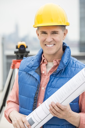 Portrait of happy male architect holding rolled up blueprint at construction siteの写真素材