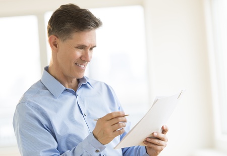 Happy mature businessman reading document in officeの写真素材