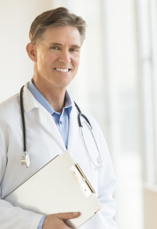 Portrait of happy mature male doctor holding clipboard while standing in clinicの写真素材