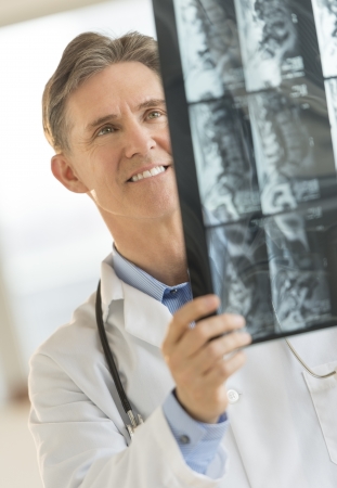Happy mature male doctor analyzing X-ray image in clinicの写真素材