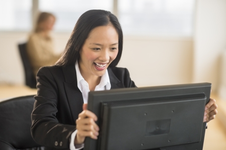 Happy mid adult businesswoman looking at computer monitor in office with female colleague sitting in backgroundの写真素材