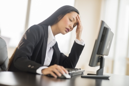 Tired mid adult businesswoman leaning while using computer at desk in officeの写真素材