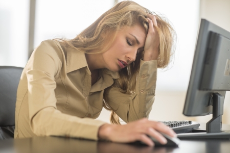Frustrated young businesswoman with hand in hair leaning on computer deskの写真素材
