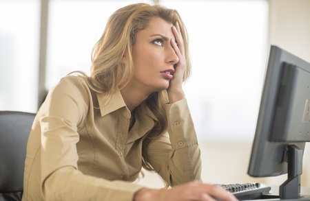 Frustrated young businesswoman looking up while sitting at computer deskの写真素材