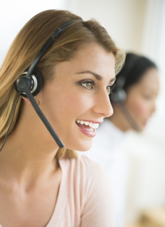 Close-up of happy female customer service representative wearing headset with colleague in backgroundの写真素材