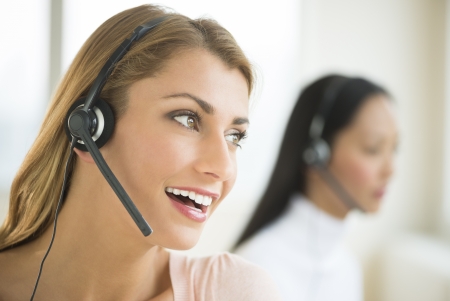 Close-up of happy female customer service representative looking away with colleague in backgroundの写真素材