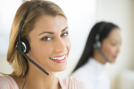 Close-up portrait of happy female customer service representative with colleague in backgroundの写真素材
