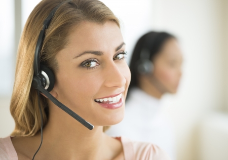 Close-up portrait of female customer service representative smiling with colleague in backgroundの写真素材