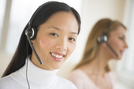 Portrait of female customer service representative smiling at office with colleague working in backgroundの写真素材