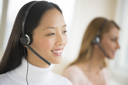 Happy female customer service representative wearing headset looking away with colleague in backgroundの写真素材