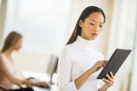 Mid adult businesswoman using digital tablet in office with female colleague sitting in backgroundの写真素材