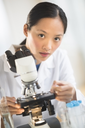 Portrait of confident mid adult female doctor using microscope in laboratoryの写真素材