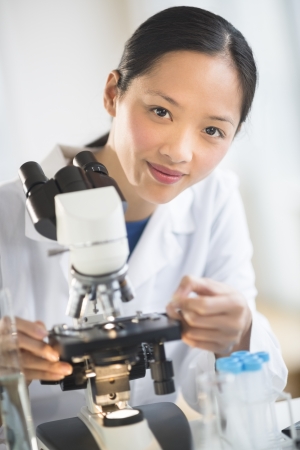 Portrait of confident mid adult female scientist smiling while using microscope in laboratoryの写真素材