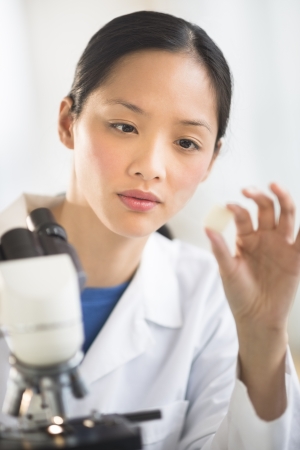 Mid adult female scientist analyzing sample with microscope in laboratoryの写真素材