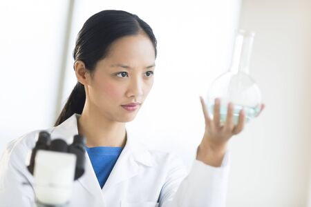 Mid adult Asian scientist analyzing chemical solution in flask at laboratoryの写真素材