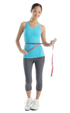 Portrait of happy Asian woman in sports clothing measuring her waistline isolated on white backgroundの写真素材