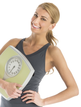Portrait of happy young woman in sports clothing holding weight scale isolated over white backgroundの写真素材