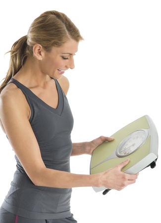 Happy young woman in sports clothing looking at weight scale against white backgroundの写真素材