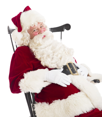 Portrait of Santa Claus with hands on stomach sitting on chair isolated over white backgroundの写真素材