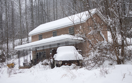 A snow covered rusty old truck sits in front of an abandoned houseのeditorial素材