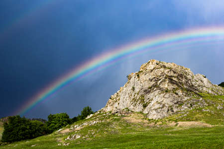 Beautiful strong rainbow against dark sky over a huge rockの写真素材