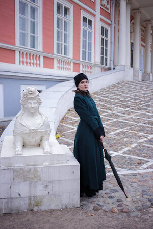 Full-length portrait of a pretty woman in vintage autumn clothes standing in front of old city buildingsの写真素材