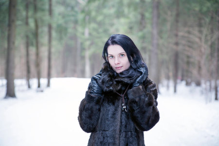 Brunette girl wearing a fur coat in winter forest