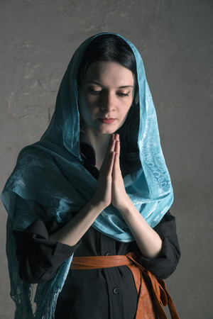 Beautiful young woman in shawl praying, studio shootの写真素材