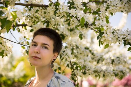 Beautiful cute girl in apple flowering trees in the summer warm dayの写真素材