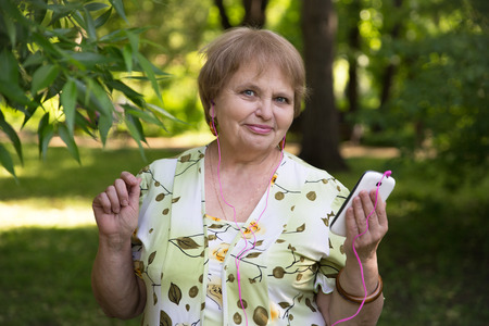 Happy senior pensioner having fun with mobile and headphonesの写真素材