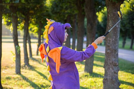 Girl wearing a carnival costume of dragon taking selfie in a parkの写真素材