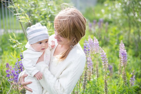 Young mother with baby at meadow lupins flowers. Soft focus on babyの写真素材