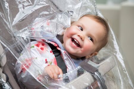 Baby girl in stroller playing with rain coatの写真素材
