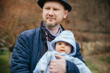 Father hugs little son outside. Wearing hat and jacket