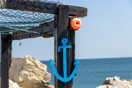 Small blue anchor on the sea shore. Sea, summer vacation and fishing concept on a sunny day