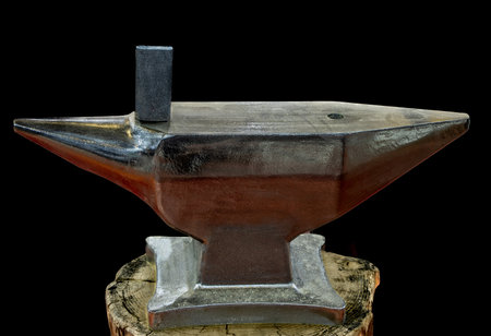 A new blacksmith anvil on a tree stump, isolated on black backgroundの写真素材