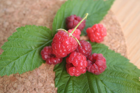 Fresh and ripe raspberries with green leaves on a wooden table