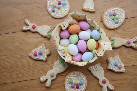Decorated Easter cookies in shape of bunny with multi colored chocolate eggs on wooden table