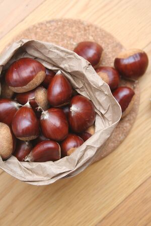 Bunch of ripe chestnuts in a paper bag on wooden background on selective focusの写真素材