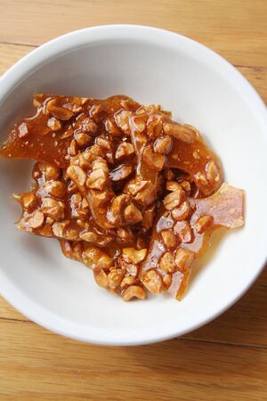Peanut brittle pieces on a white bowl on wooden tableの写真素材