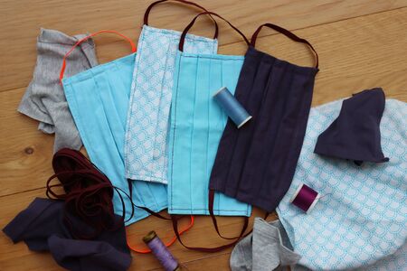 Handmade face protective masks on wooden table with fabrics. Reusable cotton face masks against coronavirus, covid-19 or flu.の写真素材