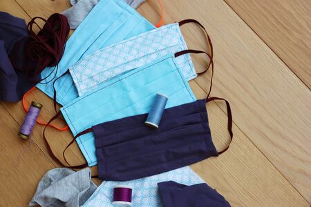 Handmade face protective masks on wooden table with fabrics. Reusable cotton face masks against coronavirus, covid-19 or flu.の写真素材
