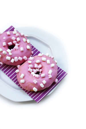 Pink glazed donuts with little marshmallow on a plate isolated on white backgroundの写真素材