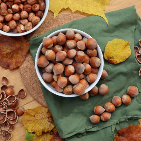 Whole hazenuts in a bowl with cracked hazenuts and autumnal leaves on wooden backgroundの写真素材