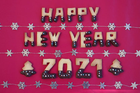 Happy New year 2021 made of cookies with chocolate glaze on red background with shiny silver...