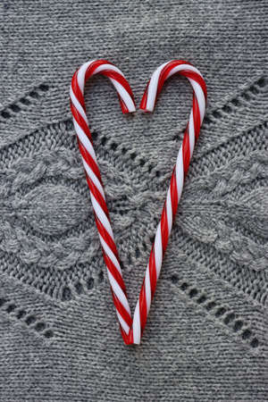 Heart shape made of candy cane ornaments on gray knitted wool background. Christmas festive backgroundの写真素材