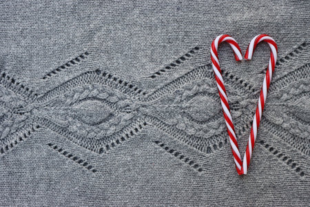Heart shape made of candy cane ornaments on gray knitted wool background. Christmas festive...