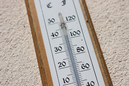 Summer heat, high temperature outdoors. Thermometer reaching 40 degrees Celsius scale on a white wall backgroundの写真素材