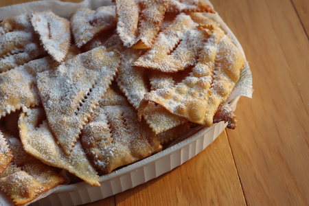 Italian Carnival pastry. Traditional carnival sweet crisp pastry deep-fried and sprinkled with powdered sugar. Chiacchere or crostoli, bugie, cenci  in a white plate on tableの写真素材