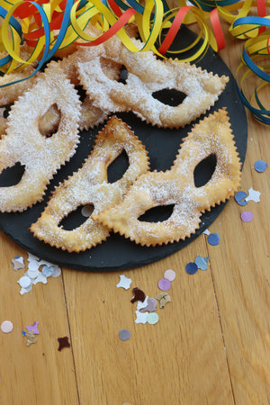 Traditional sweet crisp pastry deep-fried in shape of Carnival mask on a black slate stone plate. Chiacchere or crostoli, bugie, cenci with copy spaceの写真素材